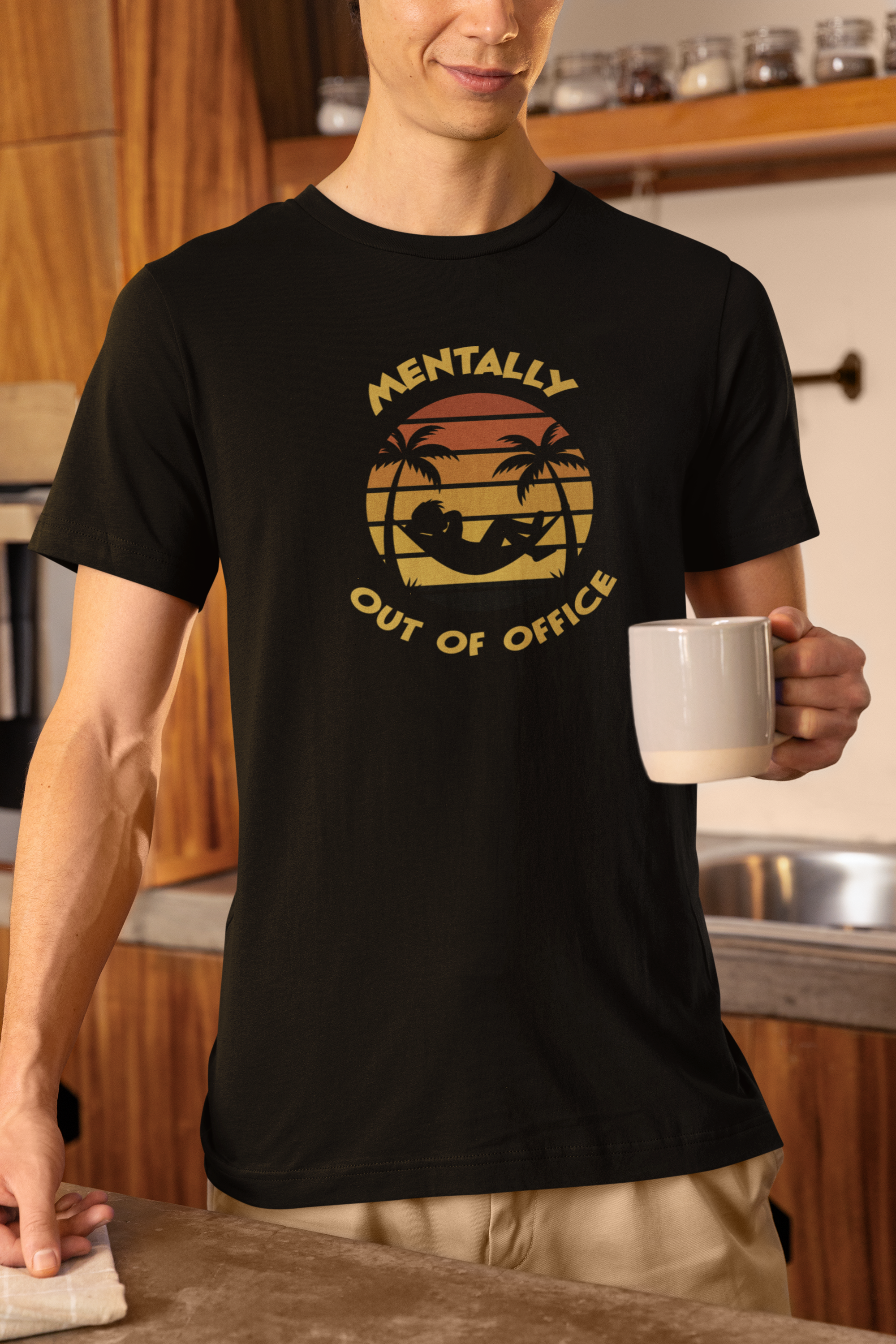 Funny Mentally Out Of Office T-Shirt Person wearing a black t-shirt with a graphic design and text, holding a mug in a kitchen.
