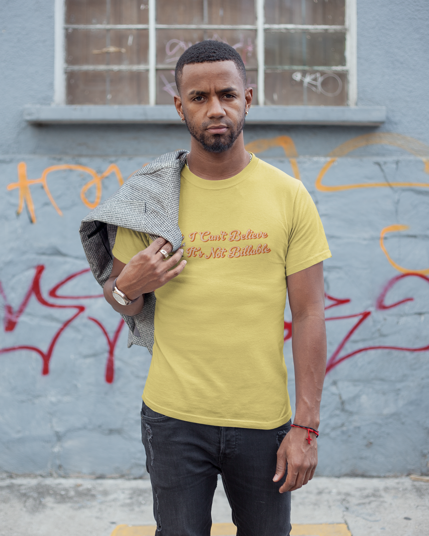 I Can't Believe It's Not Billable 100% Organic Cotton Tee Man wearing a yellow t-shirt with text, standing against a graffiti-covered wall.