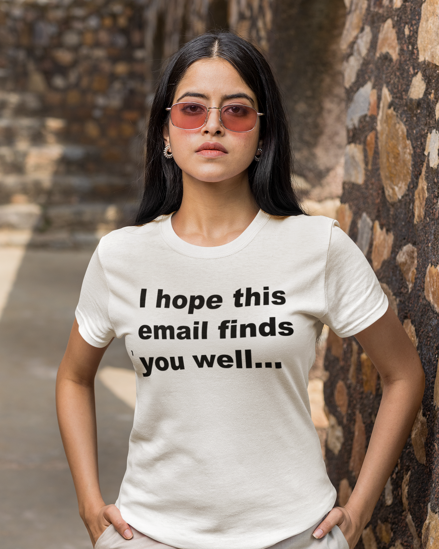 I Hope This Email Finds You Well 100% Organic Cotton T Shirt On Woman wearing a white t-shirt with text standing against a stone wall.