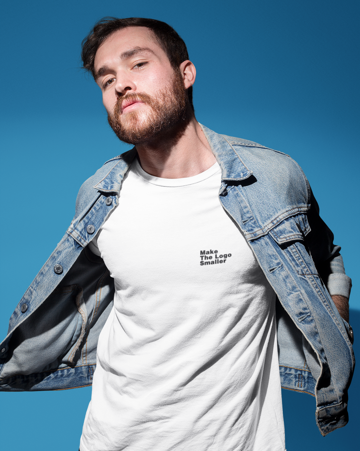 Make The Logo Smaller 100% Organic Cotton T-Shirt Man wearing a white t-shirt with text and a denim jacket against a blue sky