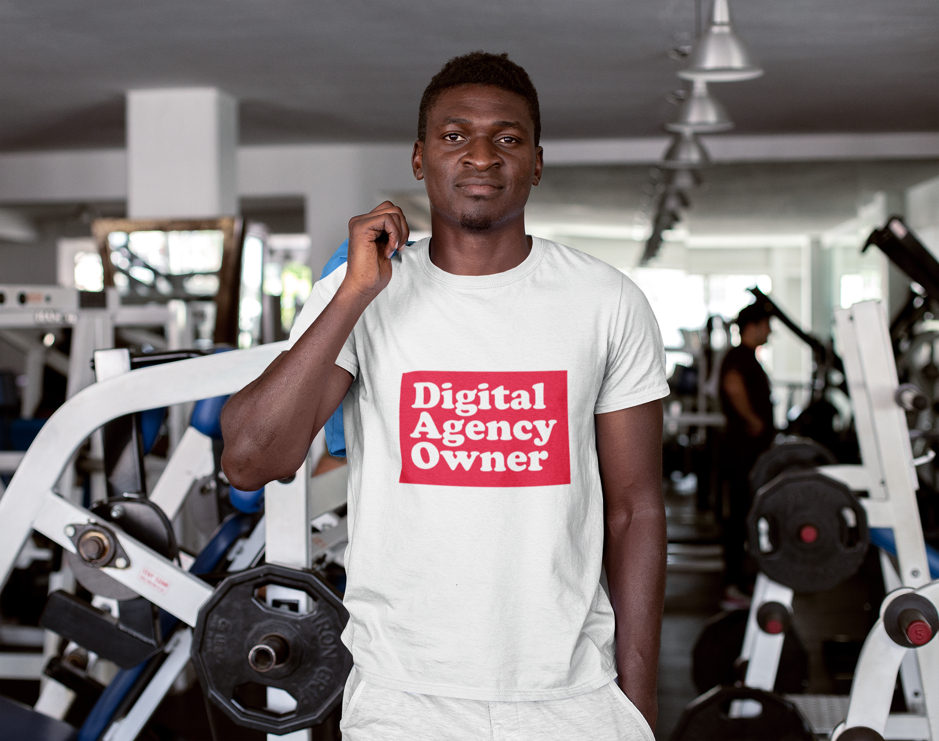 Man wearing a white t-shirt with 'Digital Agency Owner' text in a gym setting