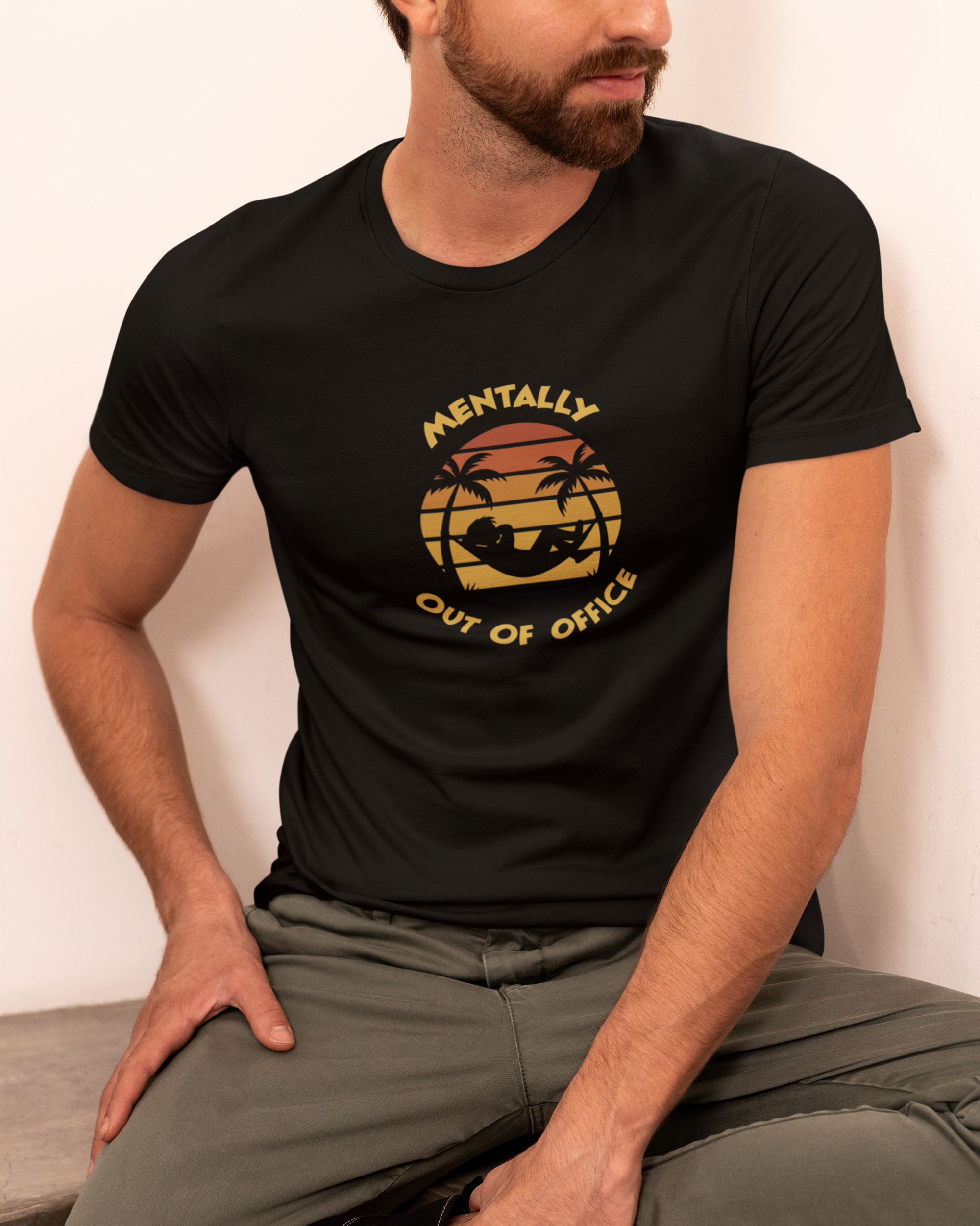 Mentally Out Of Office Tee Person wearing a black t-shirt with a graphic design sitting on a bench.