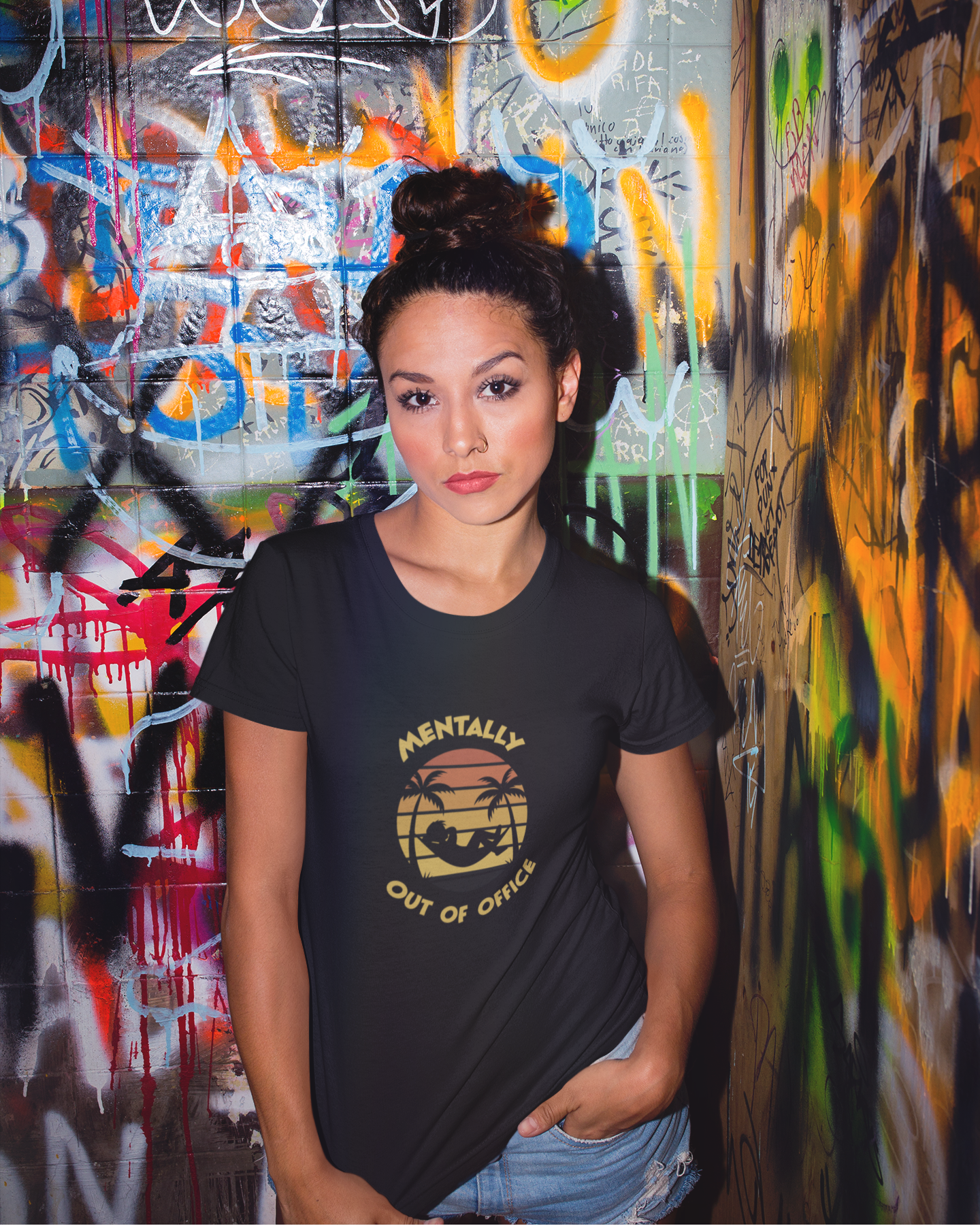 Mentally Out Of Office Tee Woman wearing a black t-shirt with text and graphics, standing in front of a colorful graffiti wall.