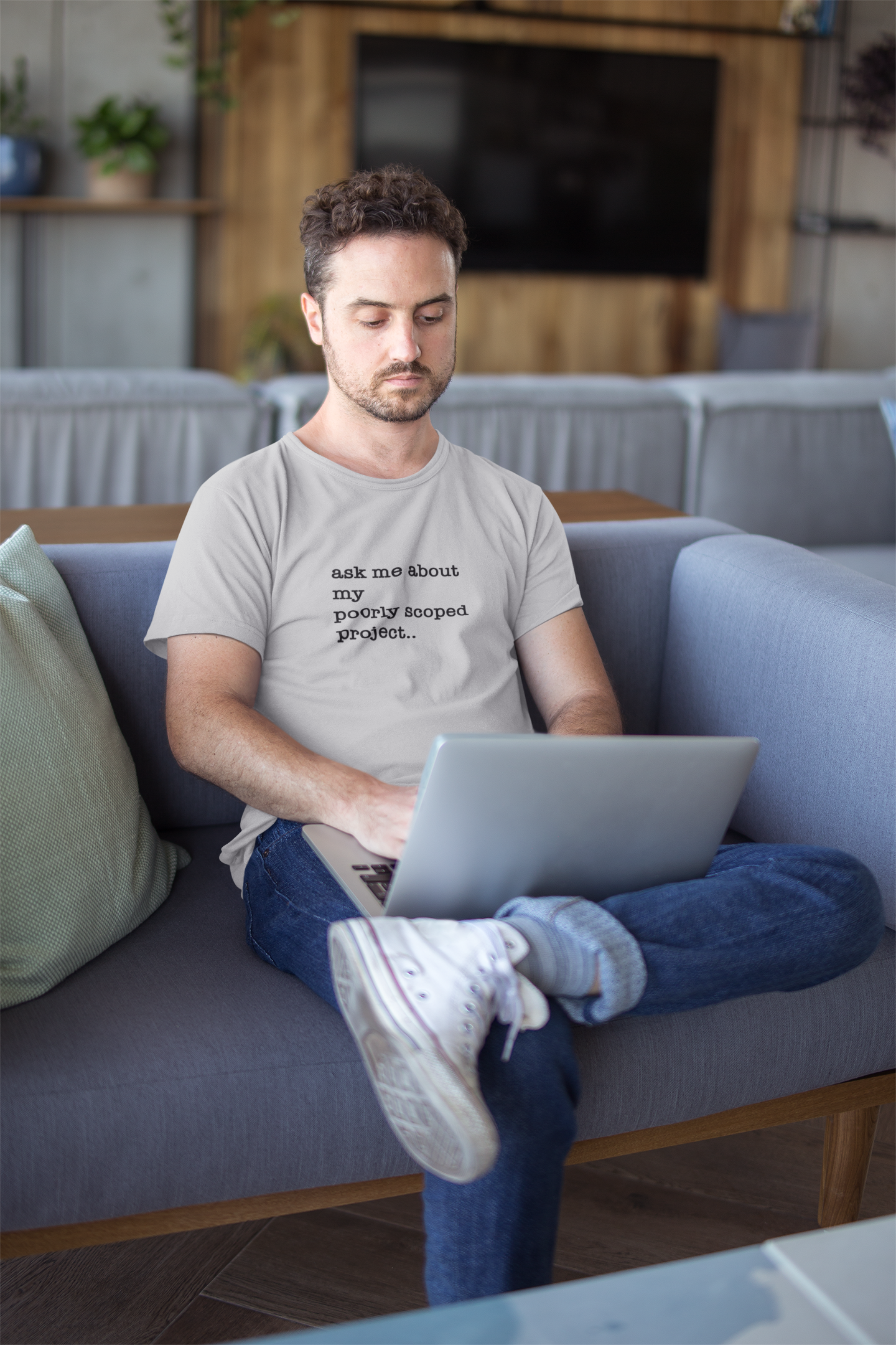 Organic Cotton Tee: Ask Me About My Poorly Scoped Project Man sitting on a couch using a laptop in a living room setting