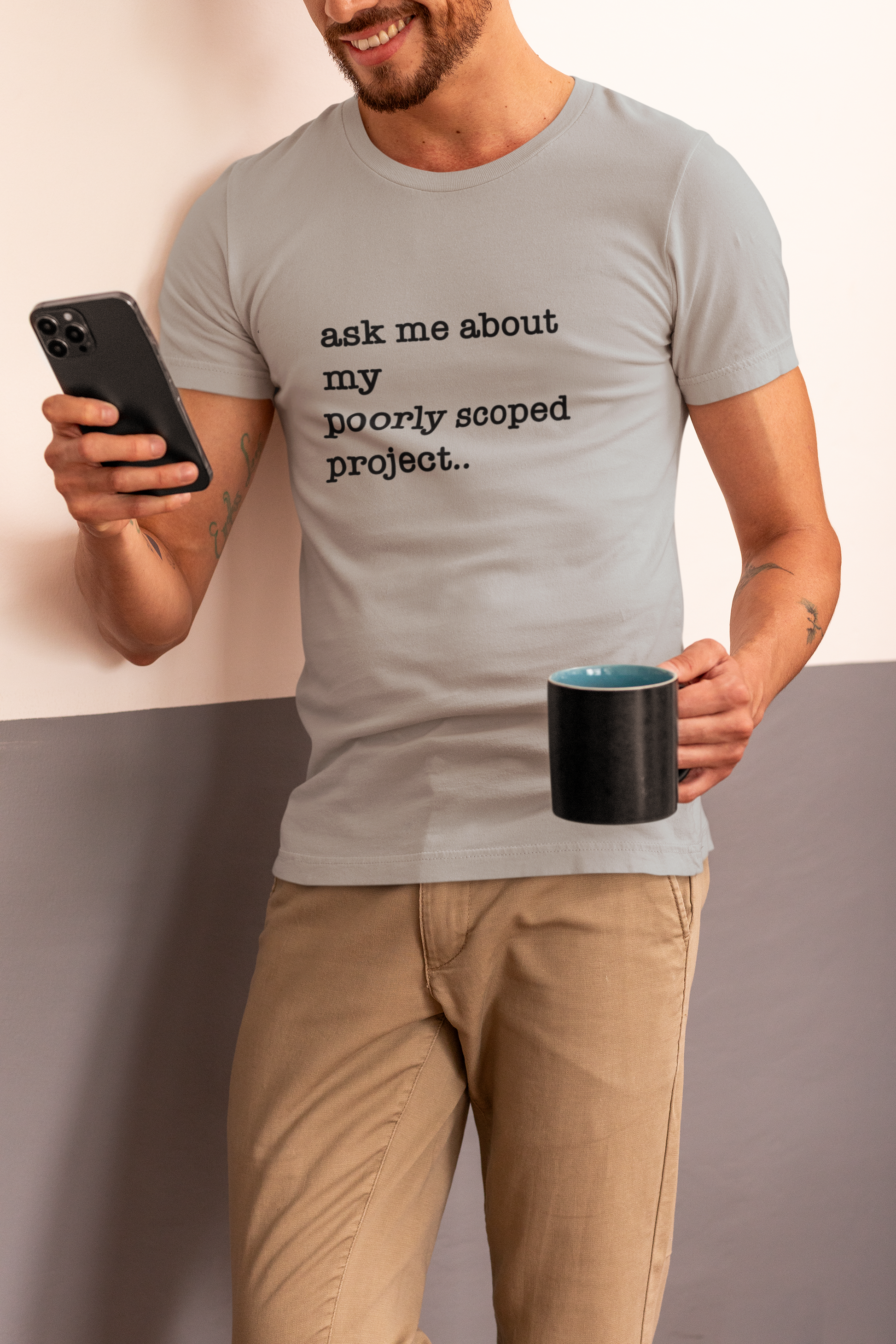 Organic Cotton Tee: Ask Me About My Poorly Scoped Project Man wearing a t-shirt with text holding a phone and mug.