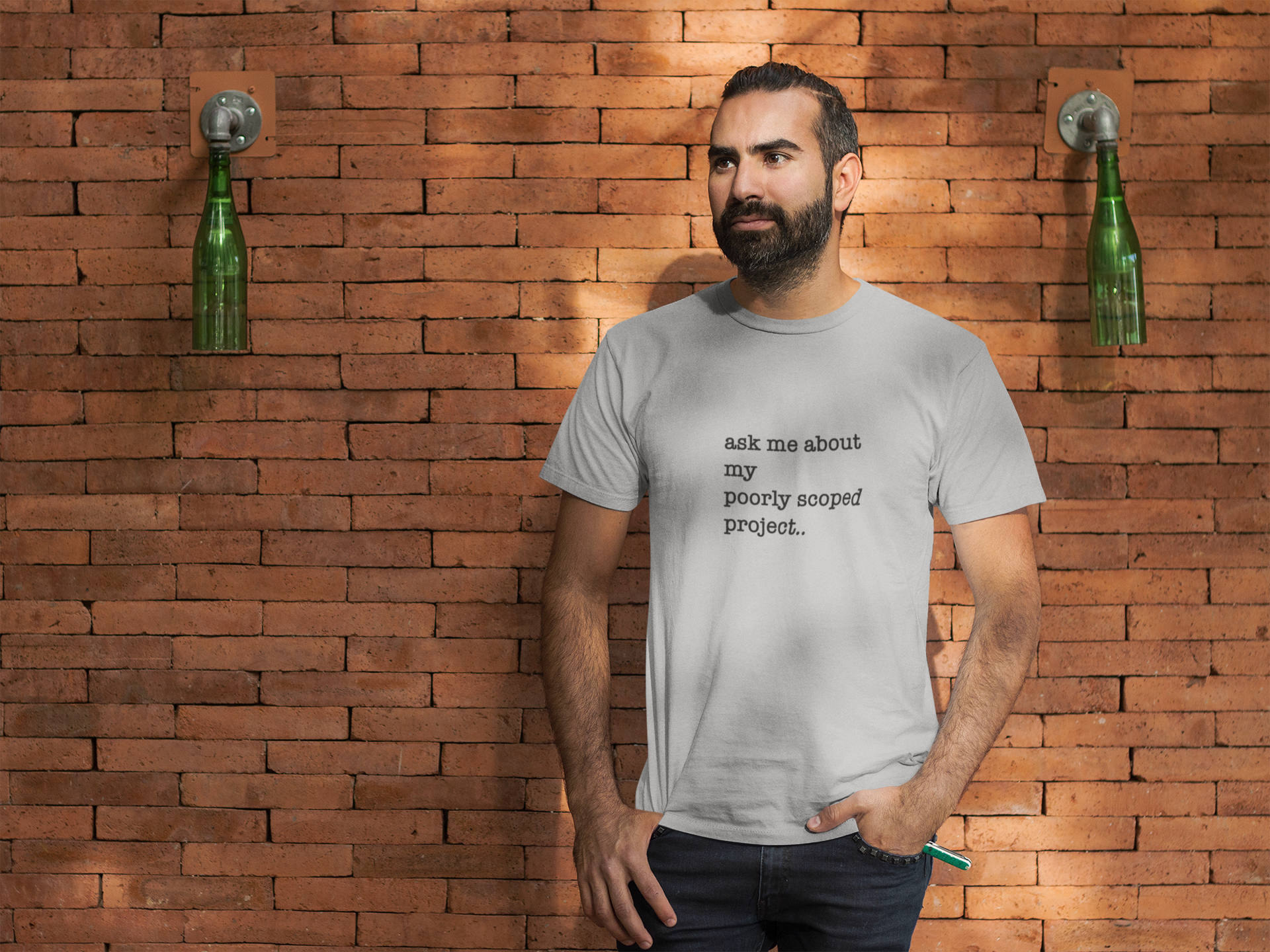 Organic Cotton Tee: Ask Me About My Poorly Scoped Project  Man wearing a t-shirt with text standing against a brick wall.