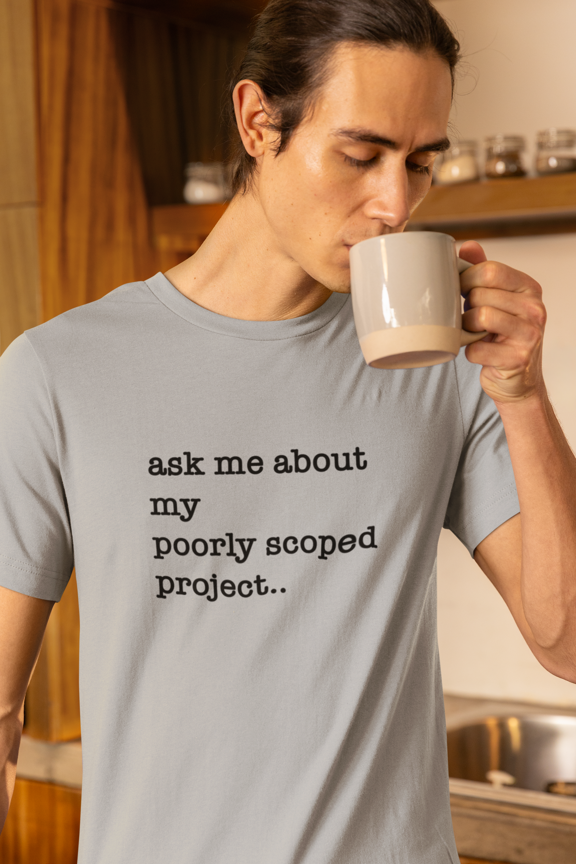 Organic Cotton Tee: Ask Me About My Poorly Scoped Project Person drinking from a mug with a shirt that says 'ask me about my poorly scoped project' in a kitchen.
