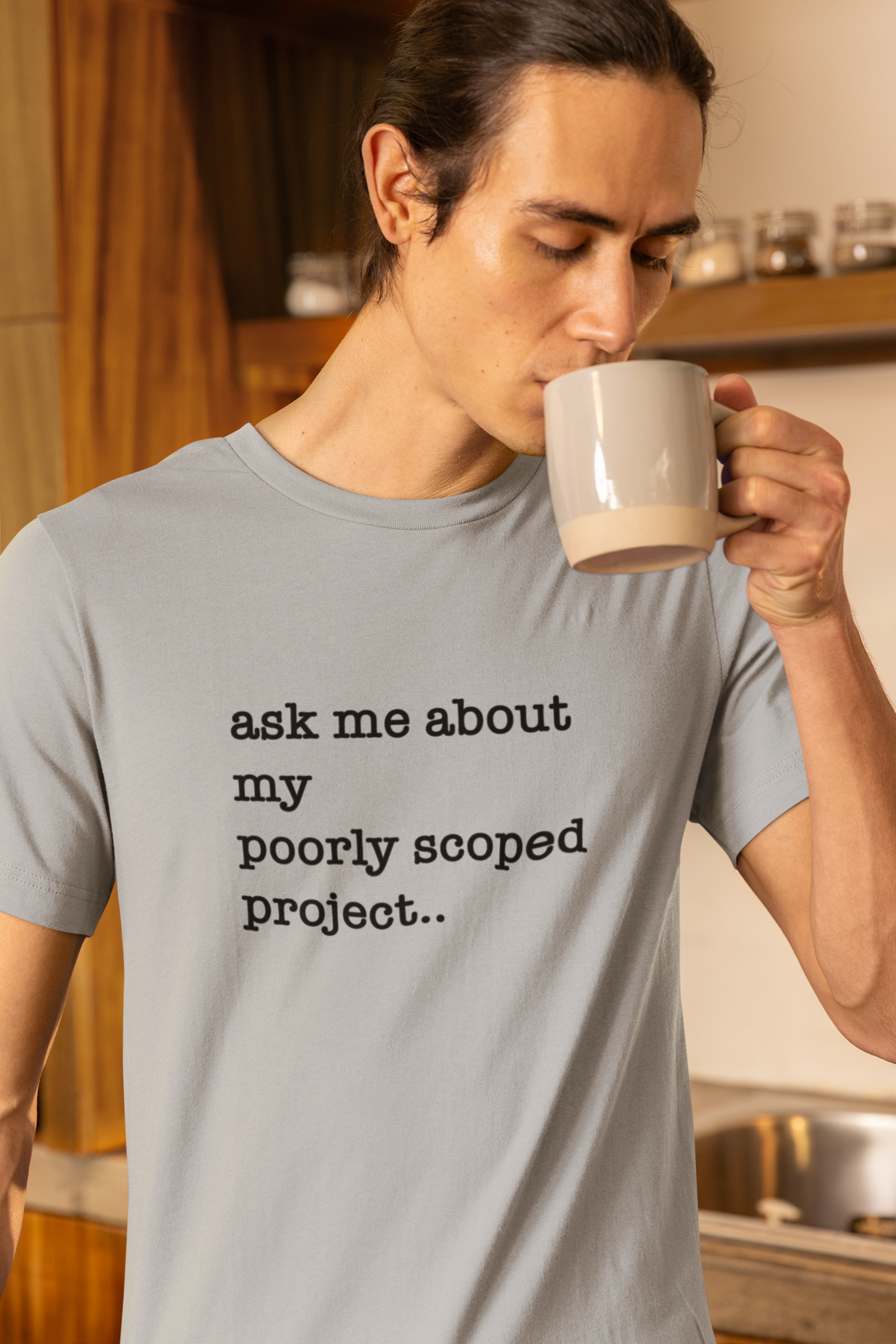Organic Cotton Tee: Ask Me About My Poorly Scoped Project Person drinking from a mug with a shirt that says 'ask me about my poorly scoped project' in a kitchen.