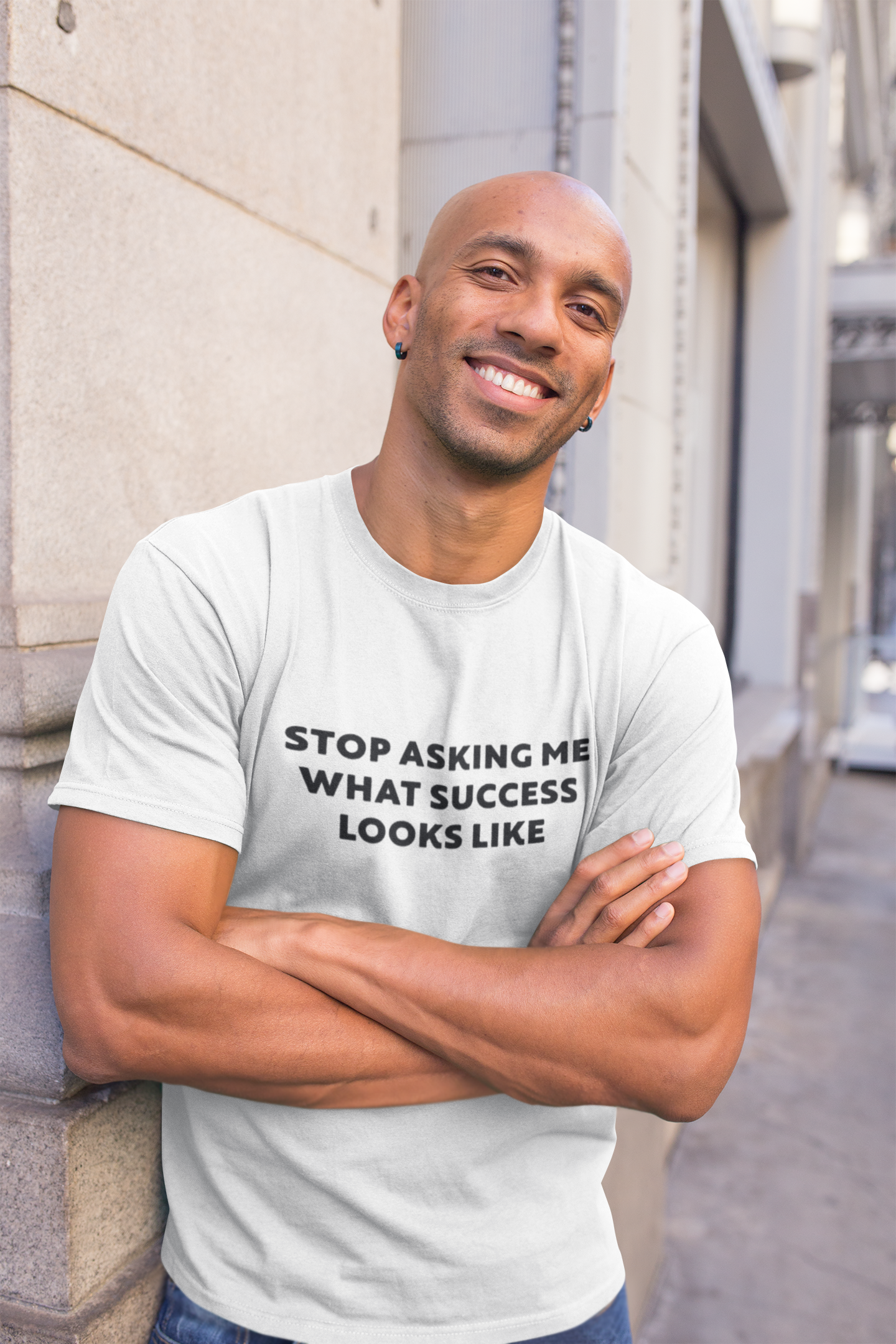 Stop Asking What Success Looks Like  T-Shirt Man wearing a white t-shirt with text standing against a building.