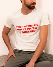 Stop Asking What Success Looks Like  T-Shirt  Person wearing a white t-shirt with red text sitting on a bench.