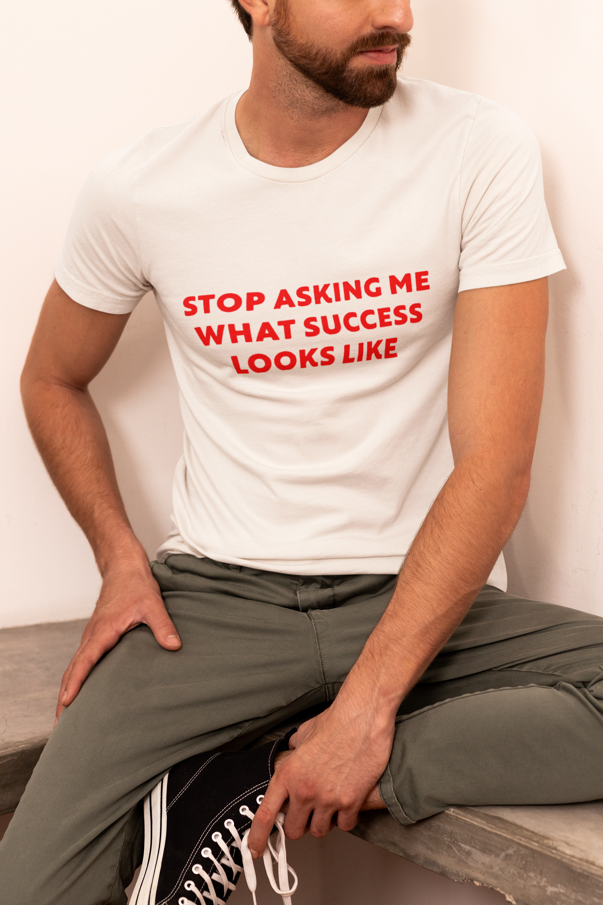 Stop Asking What Success Looks Like  T-Shirt  Person wearing a white t-shirt with red text sitting on a bench.