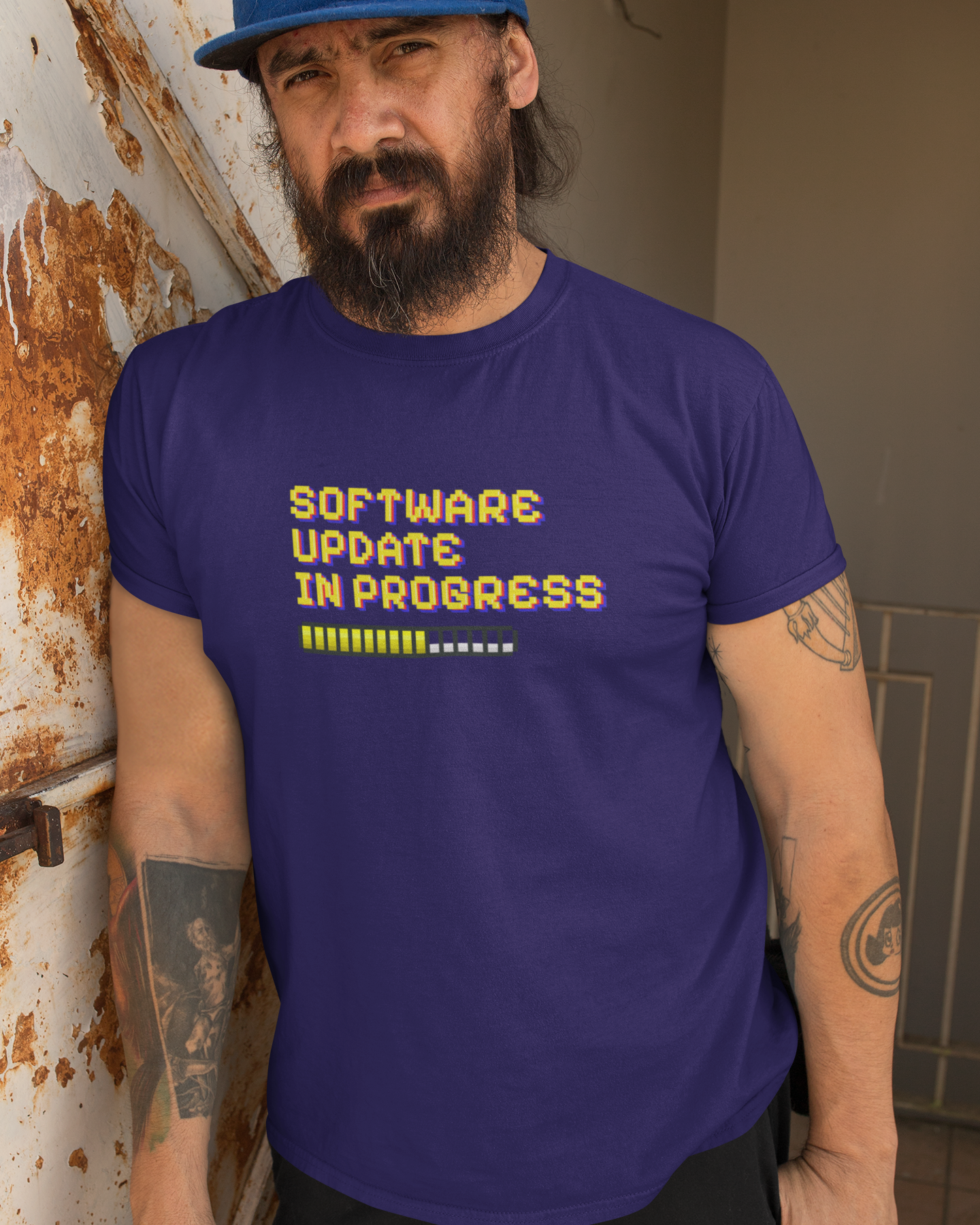 T-Shirt Humourous Slogan Software Update In Progress Man wearing a purple t-shirt with 'Software Update In Progress' text, leaning against a wall.