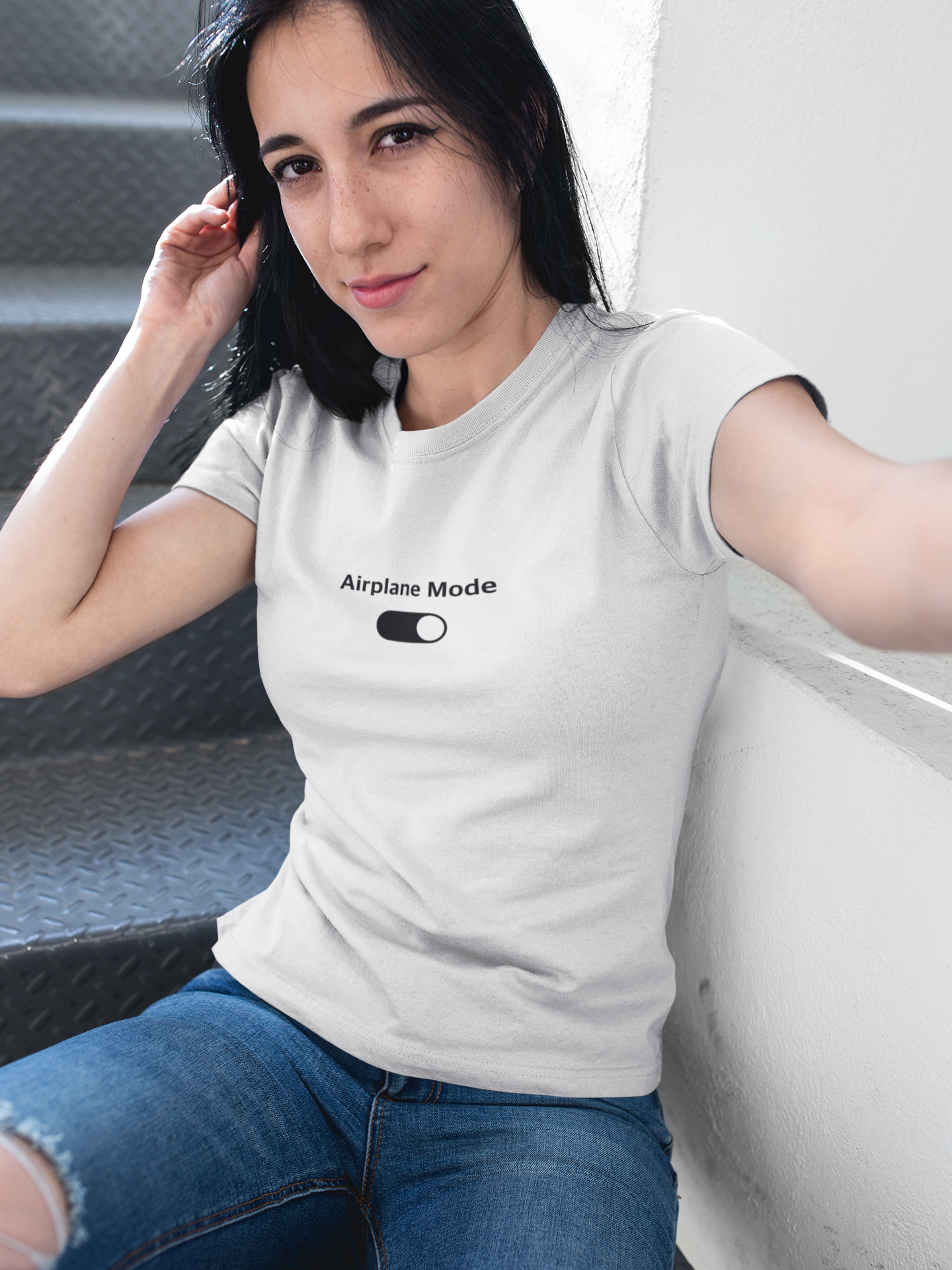 Woman wearing a white t-shirt with 'Airplane Mode' text and graphic, sitting on a couch.