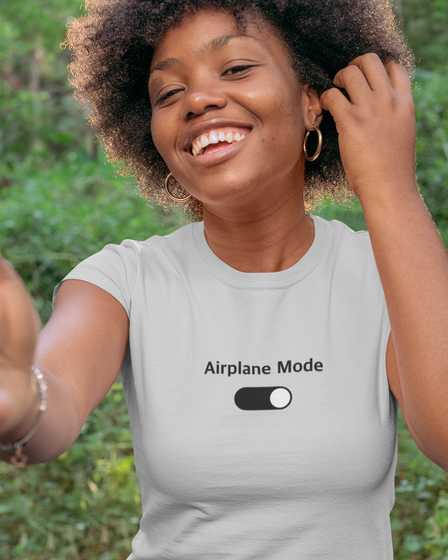 Woman wearing a light gray t-shirt with 'Airplane Mode' text and toggle graphic, outdoors.