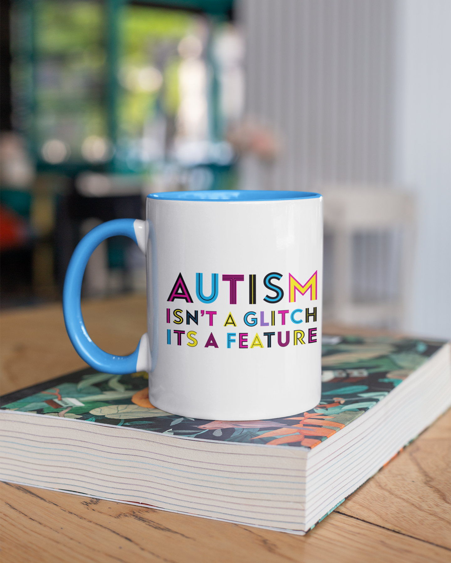 Mug with 'Autism isn't a glitch, it's a feature' text on a stack of books.