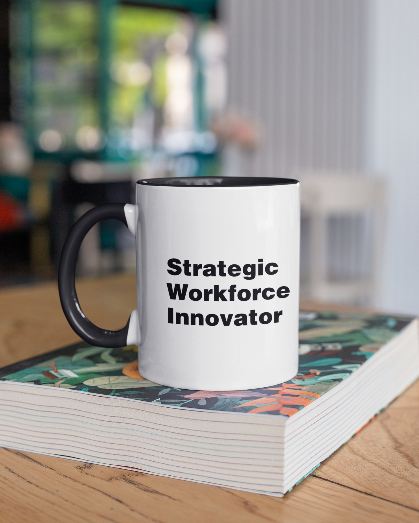 Mug with 'Strategic Workforce Innovator' text on a stack of books in an office setting