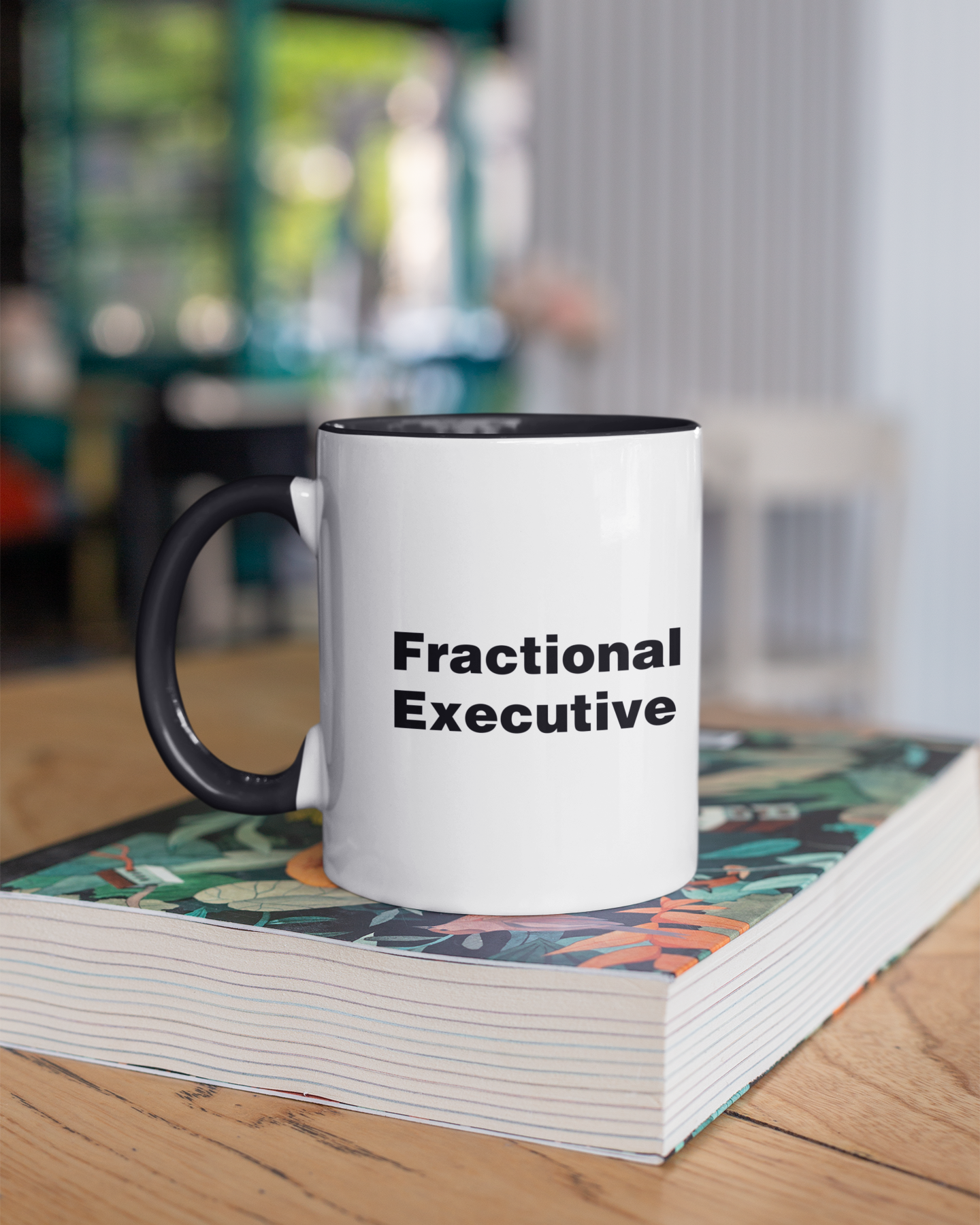 Mug with 'Fractional Executive' text on a stack of books in an office setting