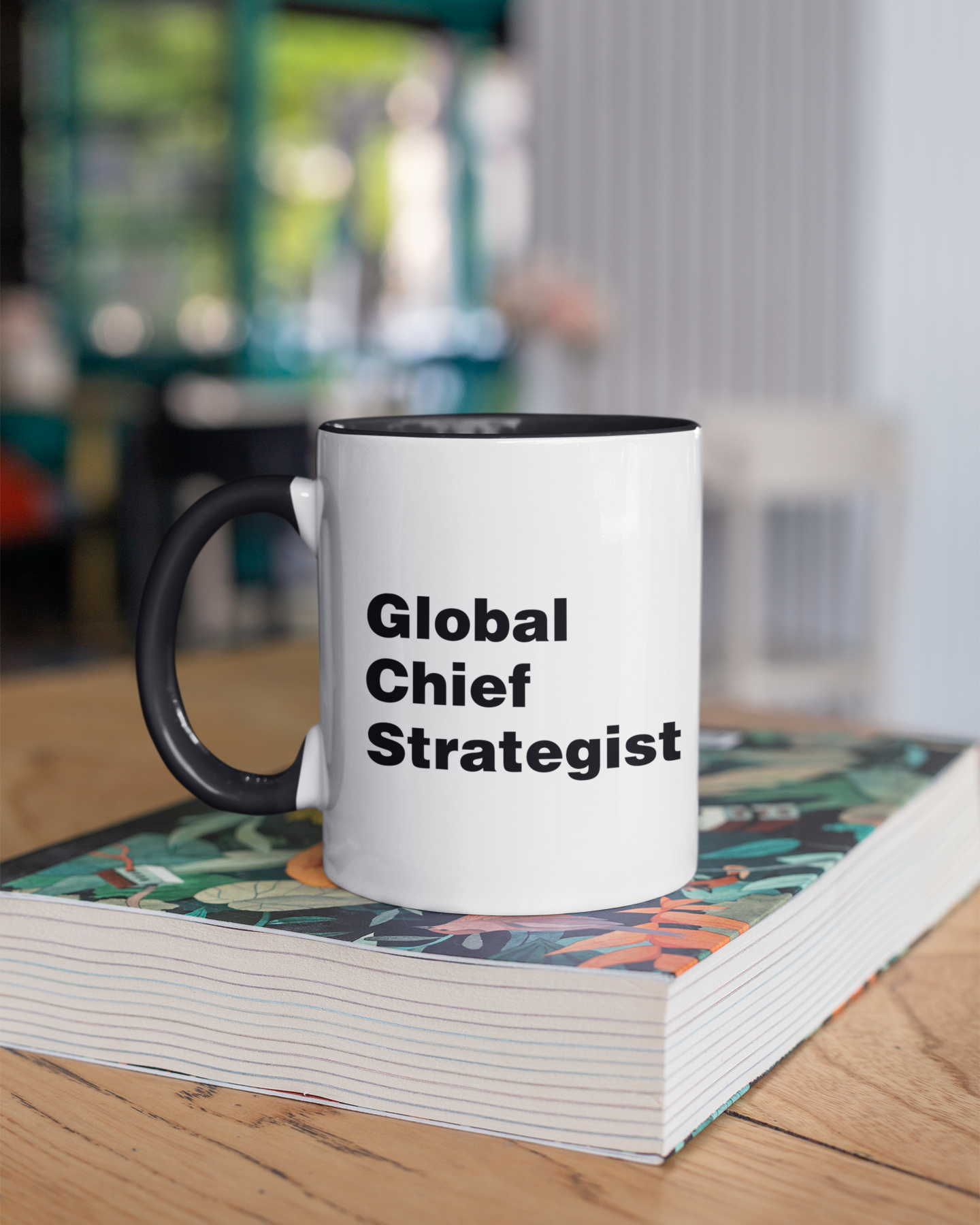 Mug with 'Global Chief Strategist' text on a stack of books in an office setting