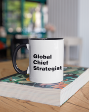 Mug with 'Global Chief Strategist' text on a stack of books in an office setting