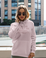 Woman wearing a light pink hoodie with text, standing in front of a modern building.